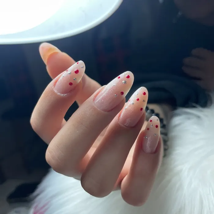 Unghie a mandorla nude con piccoli pois rossi, su pelo bianco